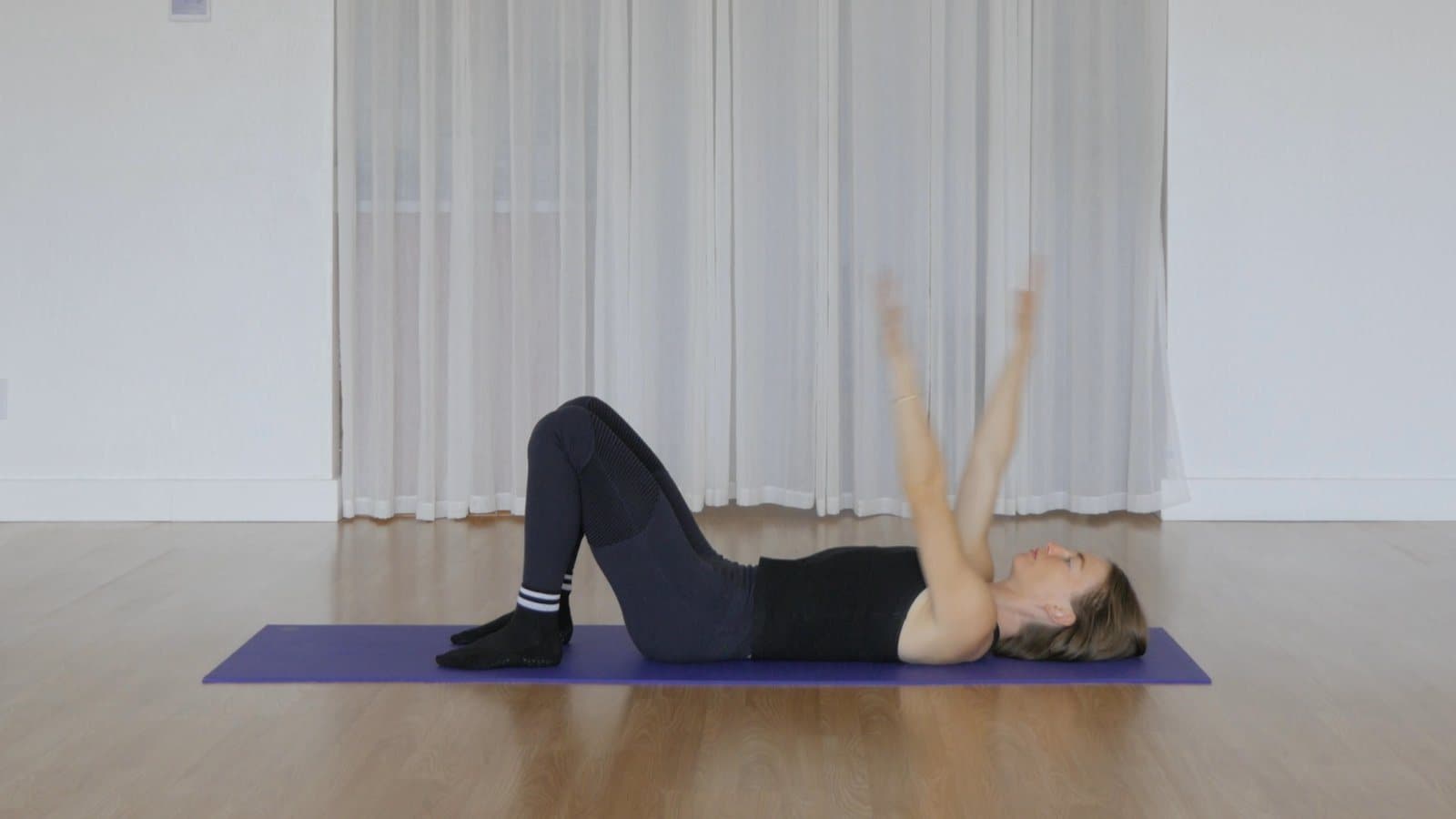 Lying on the back with knees bent and both arms reaching overhead to the floor