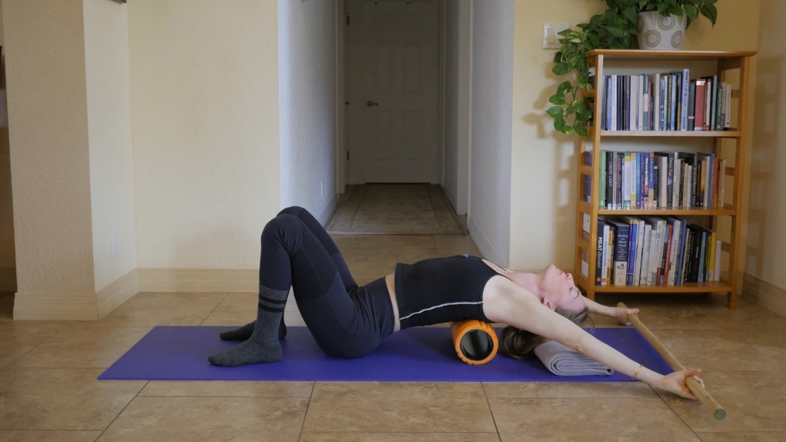 Lying back over a foam roller, reaching a dowel overhead to open the chest